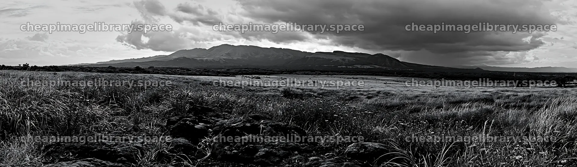 Kumamoto volcanic meadow with dark rock foreground and clouds – image library 14762x4268