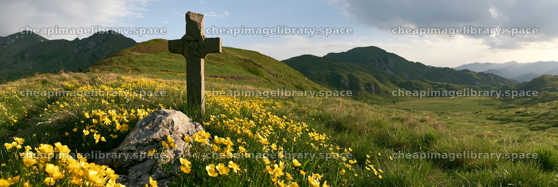 Christian cross in a meadow with yellow flowers in the mountains – image library 13690x4602
