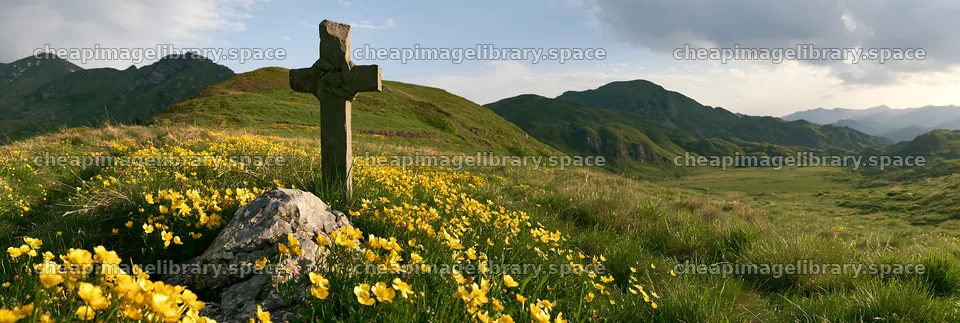 Christian cross in a meadow with yellow flowers in the mountains – image library 13690x4602