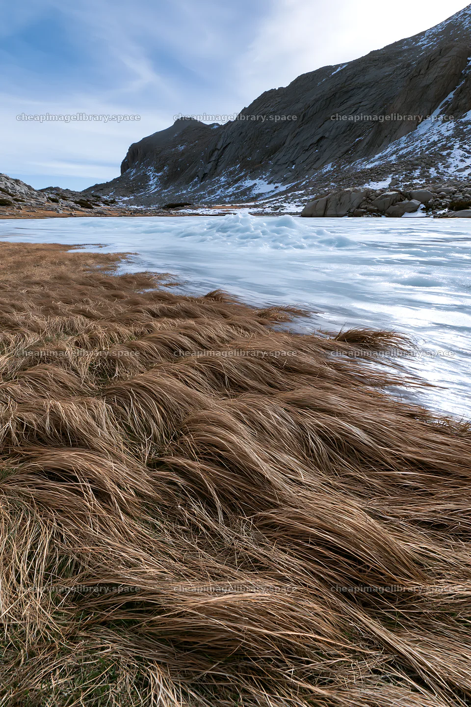 Frozen tarn meadow with grass and ice near rocky hillside – image library 6480x9722