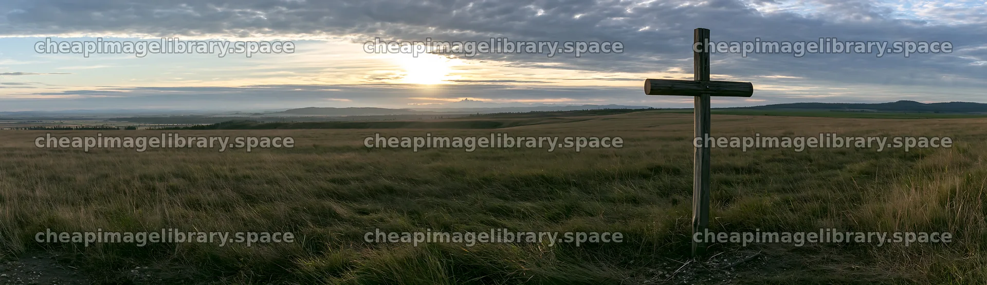 Christian cross in meadow at sunrise with cloudy sky – image library 14762x4268