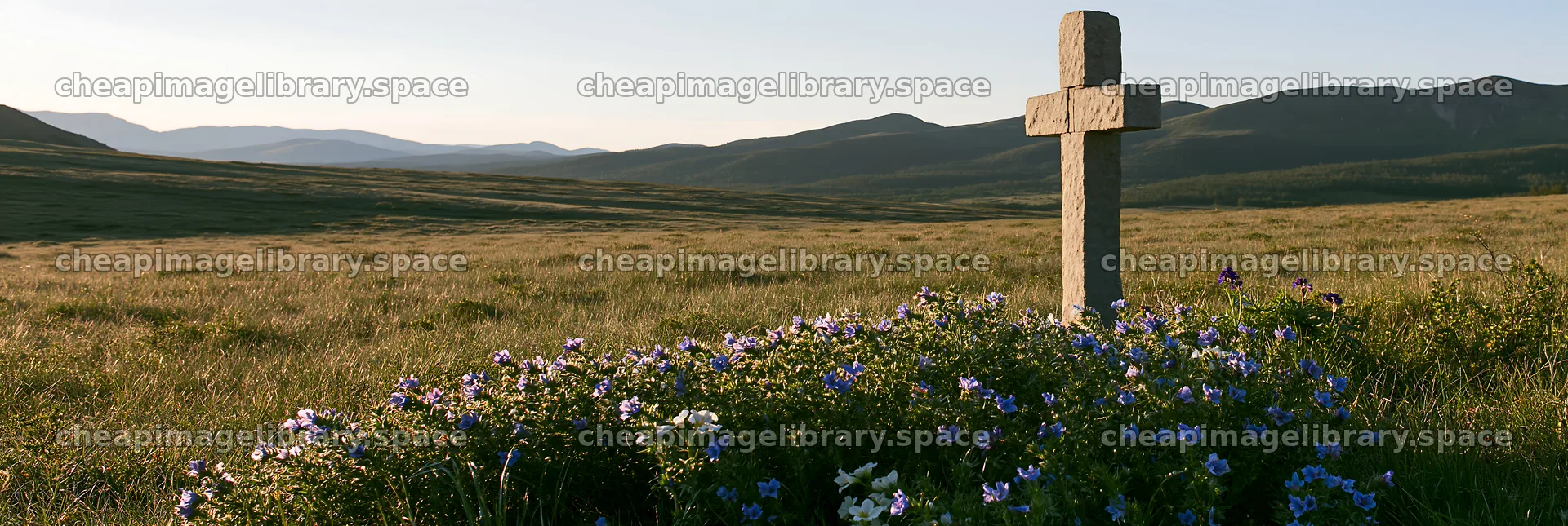 Simple cross in meadow with flowers and mountains in background – image library 13690x4602